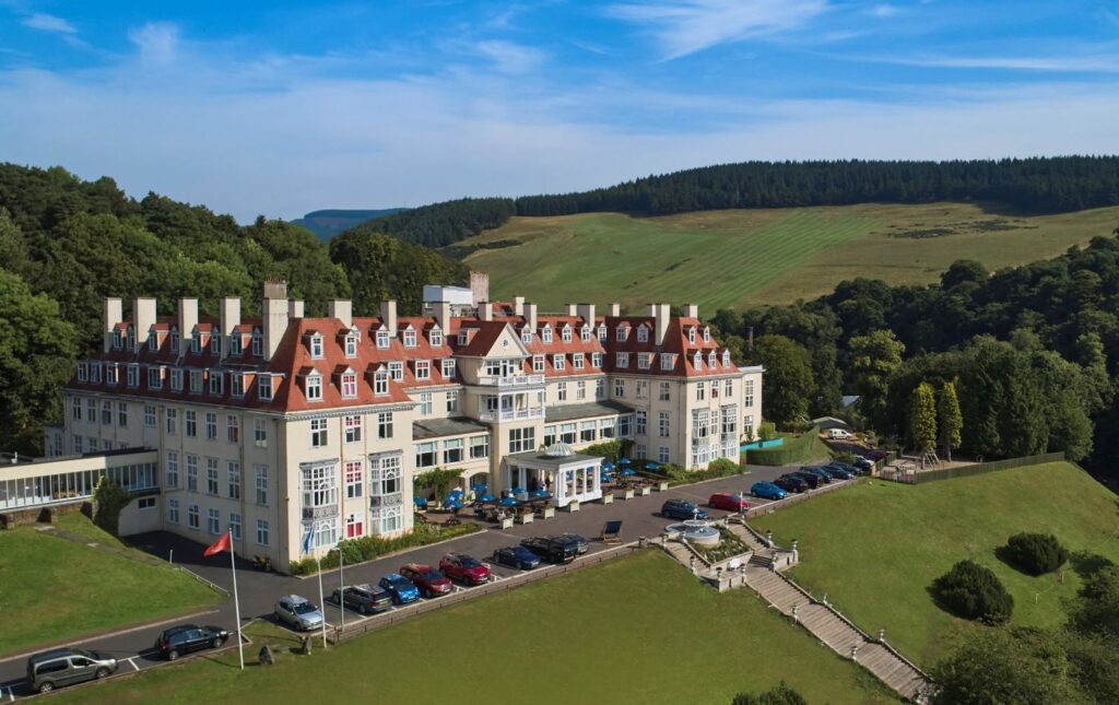 External view of the Peebles Hydro, a hotel, set with blue sky and green rolling hills. The hotel will be the venue for the South of Scotland THistle Awards 2024.